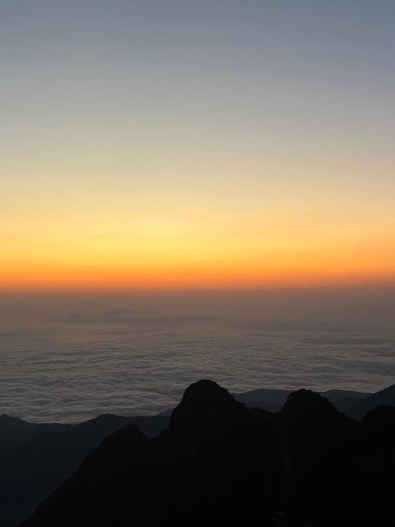 Silhueta dos picos da Mantiqueira com pôr do sol laranja e mar de nuvens