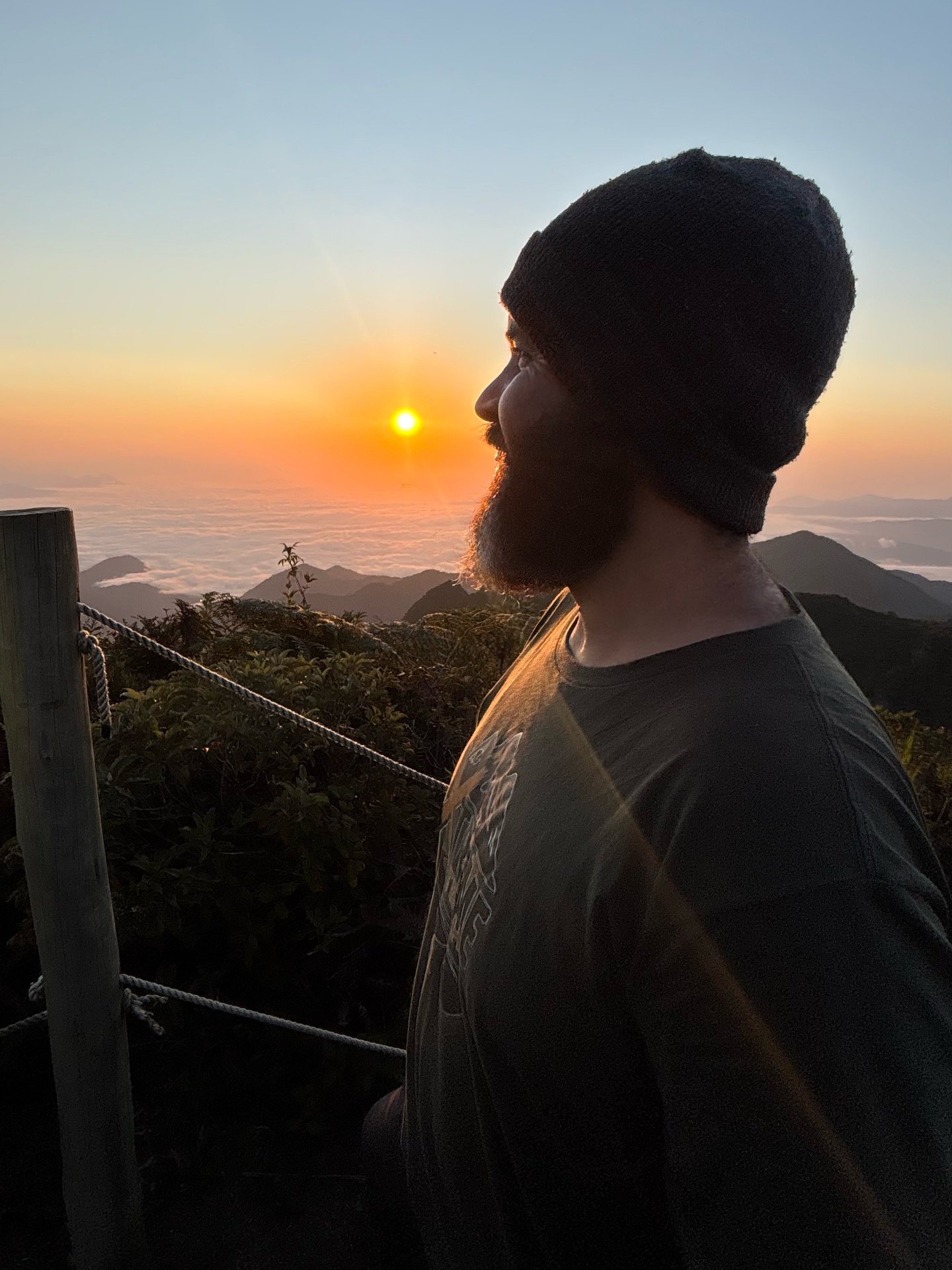 Aventureiro em silhueta contemplando o nascer do sol sobre o mar de nuvens no cume do Pico do Marins
